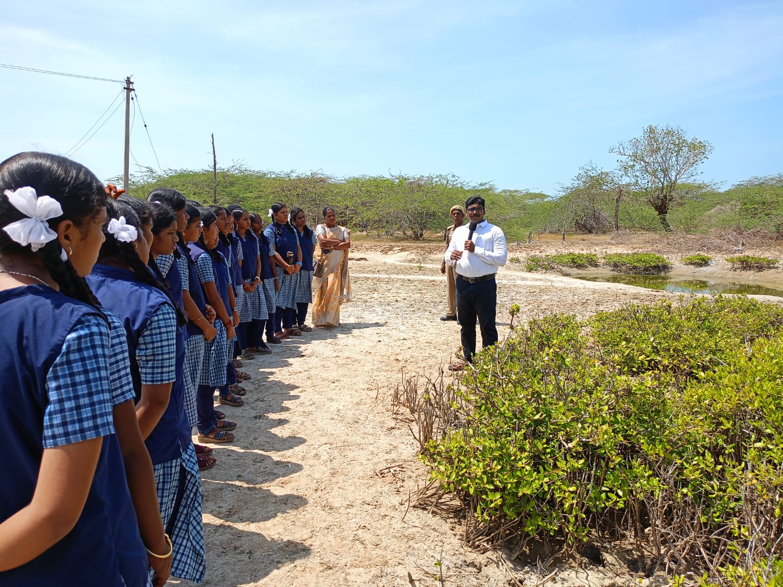 A group of school students learning outdoors beside coastal vegetation with an instructor.