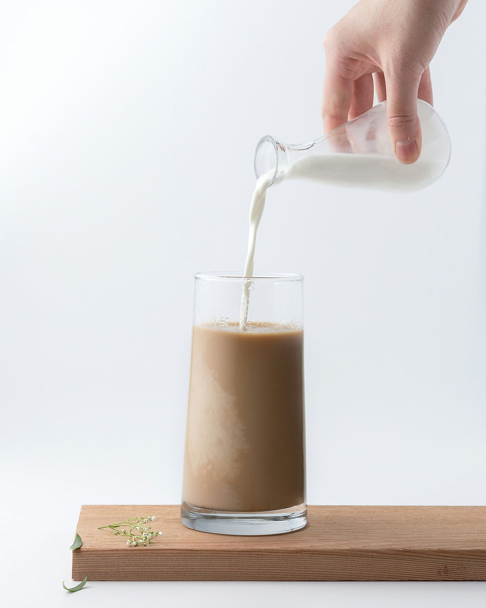 A hand pouring milk into a clear glass of chocolate milk