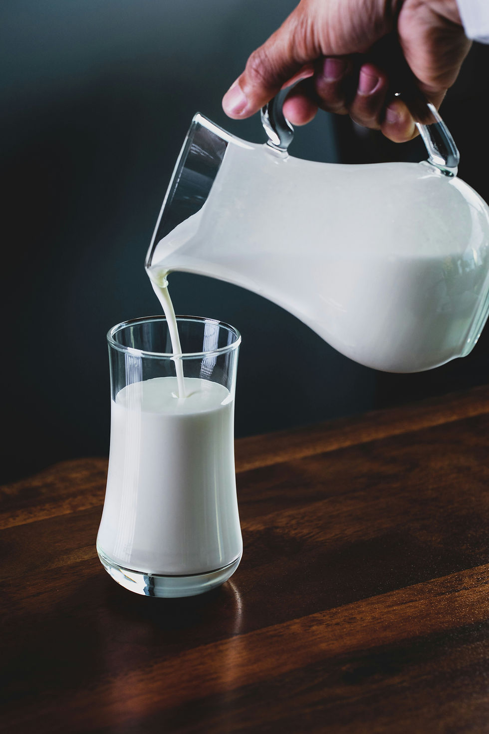 A glass being filled of milk from a glass pitcher