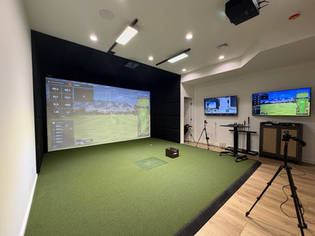 Modern TrackMan home golf simulator with black padded enclosure, turf, dual wall displays and swing-analysis cameras
