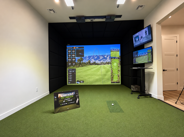 Wide view of a modern TrackMan golf simulator room with impact screen, hitting turf and wall-mounted analysis displays.