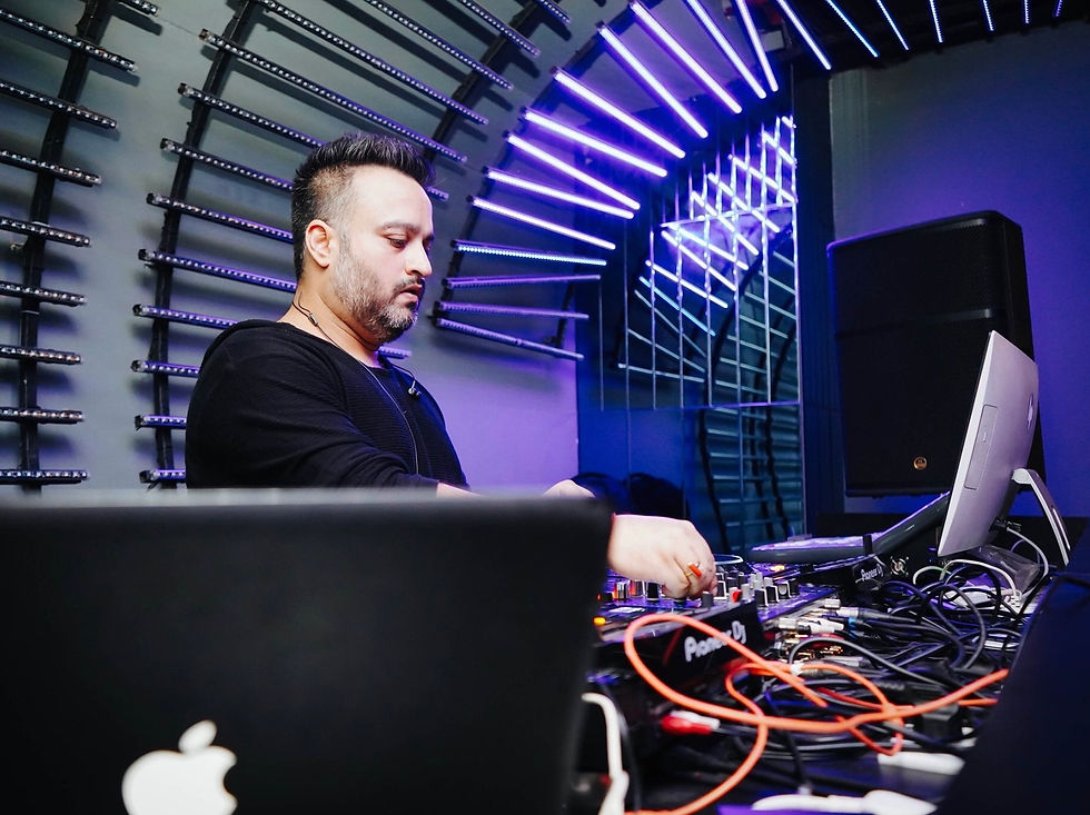 DJ Anish Anand mixing differnt genres of music at a deck under purple-lit, futuristic arch with cables and equipment. Focused expression, vibrant club atmosphere. Open Format Djing in Club Ministry Of Sound Noida
