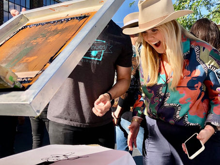 Guests gathered around a live screen printing station, smiling as they print custom t-shirts at an event.