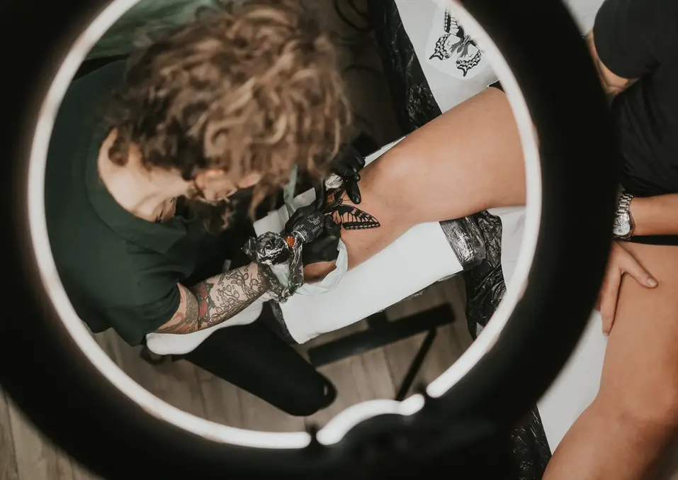 Tätowierer bei der Arbeit an einem Tattoo am Bein unter Ringlicht.