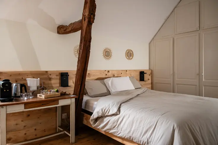 Tweepersoonsbed in Descartes-kamer met houten hoofdbord en zicht op kastenwand
