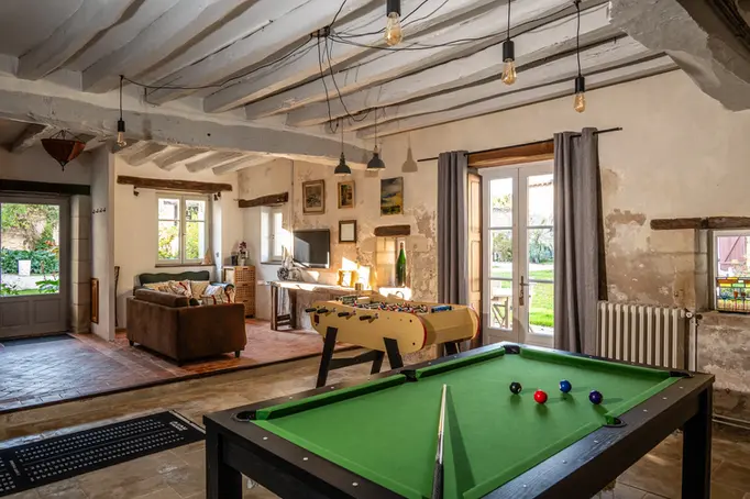 Ontspanningsruimte met pooltafel, kickertafel, zithoek met sofa’s en ramen met zicht op de tuin
