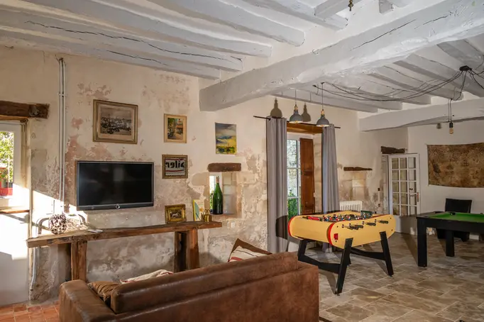 Recreatieruimte met pooltafel, kickertafel, televisie aan de muur, zithoek en zichtbare plafondbalken
