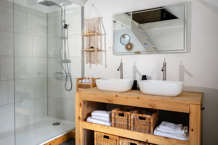 Badkamer met inloopdouche en dubbele wastafel op houten meubel
