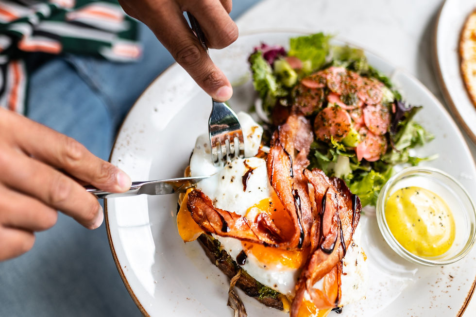 Person holding a knife and fork cutting an open face egg sandwich, portion control