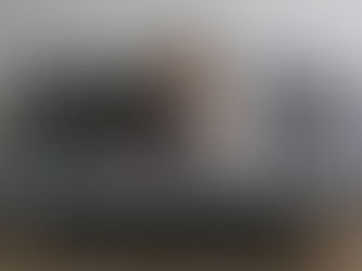 Woman in beige sweater and jeans sitting on a gray sofa, looking at a smartphone. The setting is minimal and calm.