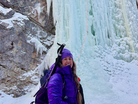 Woman wearing purple jacket in front of a frozen waterfall