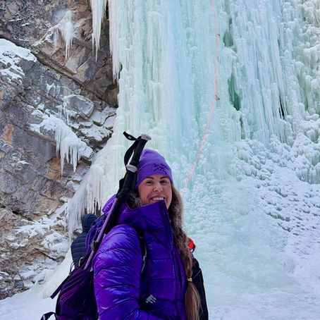 Woman wearing purple jacket in front of a frozen waterfall