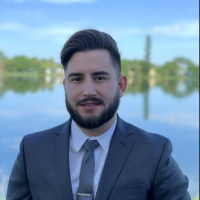 Professional headshot of an electrical engineer wearing a suit at an outdoor job site.