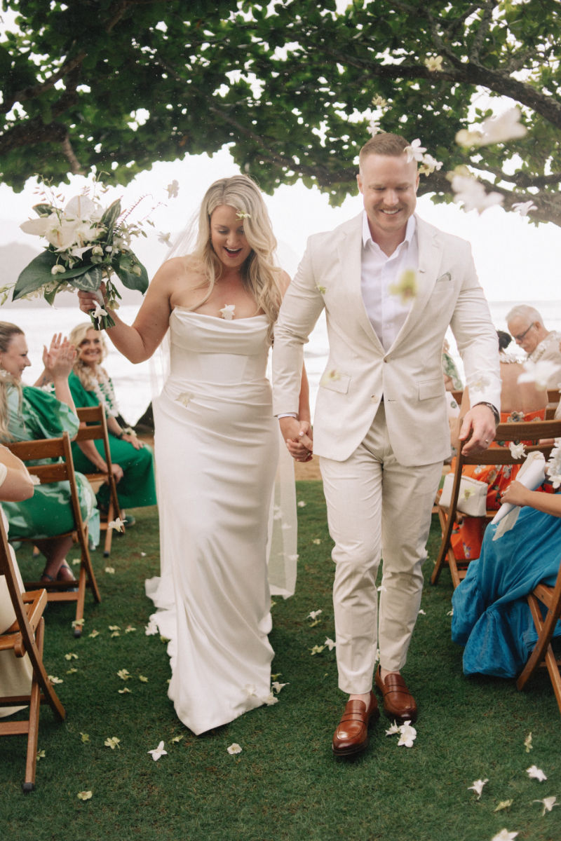 Destination wedding planner captures couple walking down aisle, guests tossing petals, joyful outdoor ceremony moment