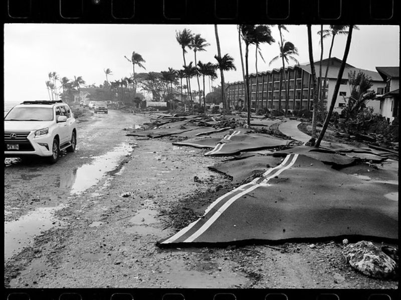 Hurricane recovery on Kauai showing damaged roads, fallen debris, palm trees, and buildings after the storm.