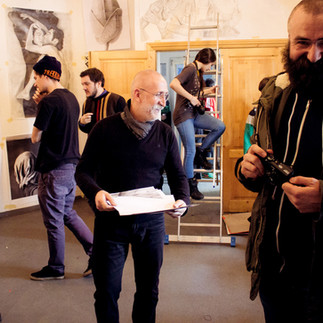 Profesorul și artistul Valeriu Mladin în dialog cu studenții săi din Departamentul Foto-Video al UNArte București. Fotografie care surprinde procesul de învățare prin desen, culoare și compoziție, în cadrul unei pedagogii bazate pe reflecție și experiment vizual. Professor and artist Valeriu Mladin in dialogue with his students from the Photo-Video Department at UNArte Bucharest. Photograph capturing the learning process through drawing, color, and composition, within a pedagogy grounded in reflection and visual experimentation.