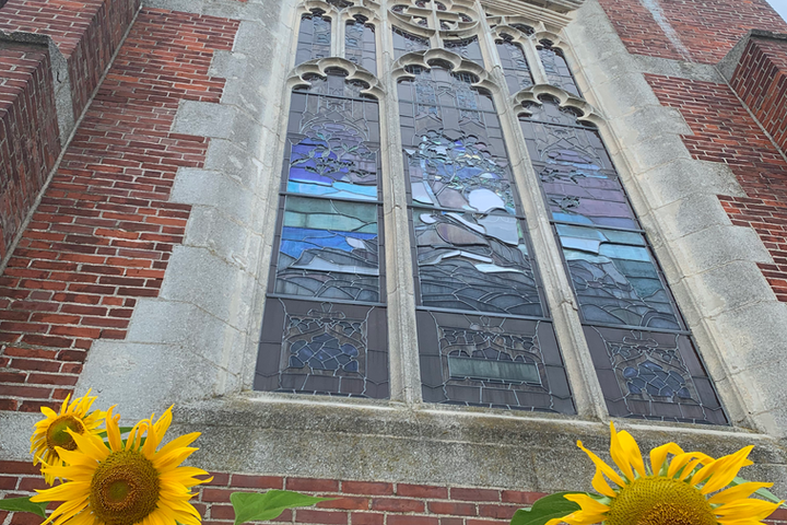 A stained glass window is framed by yellow sunflowers.