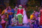 The Grinch, dressed in a Santa suit, poses on stage with the Whos in front of a brightly lit Christmas tree during the Grinchmas show at Universal Orlando.
