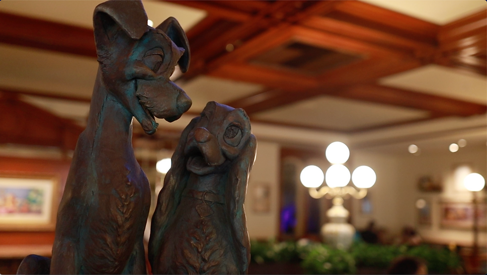Bronze dog sculptures gaze affectionately at each other in a warmly lit restaurant with wooden ceiling and glowing chandeliers.