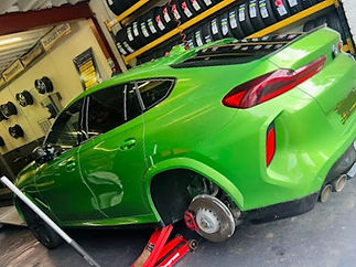 Green car on red jack missing rear wheel in garage