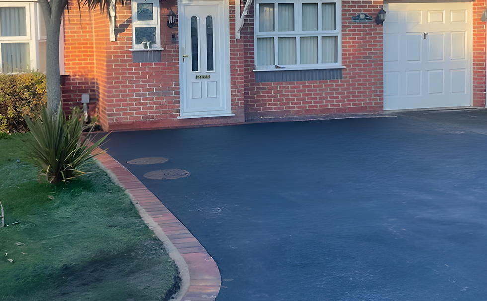 Tarmacadam driveway of red brick home, trees and bushes to the left of driveway