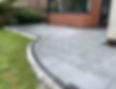 Grey block paved patio with a curved section, dark grey brick border