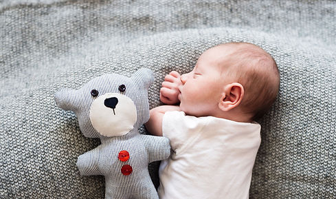 Das Bild zeigt einen schlafenden Säugling neben einem Teddy Bär