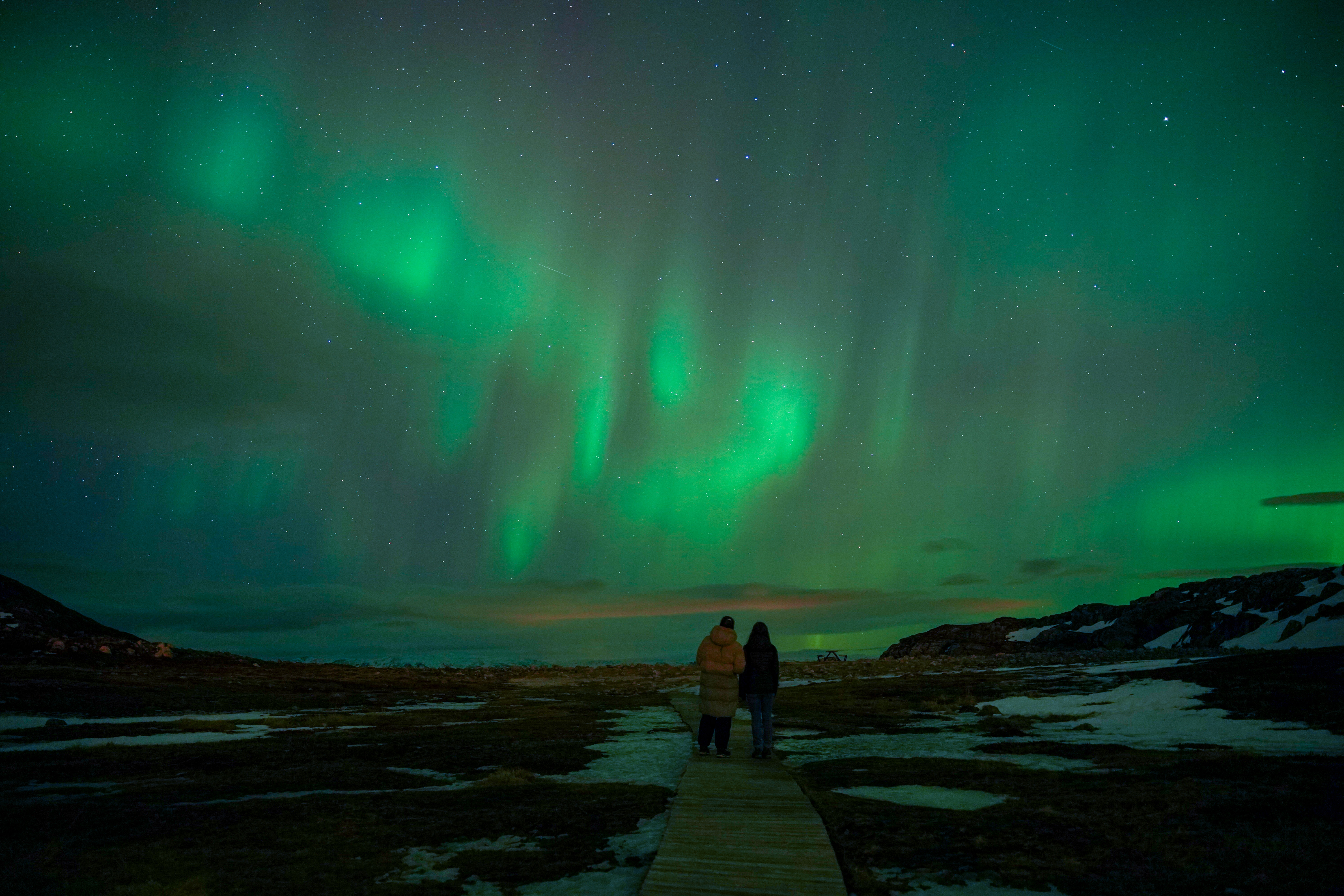 Two women standing at the sea under the northern lights
