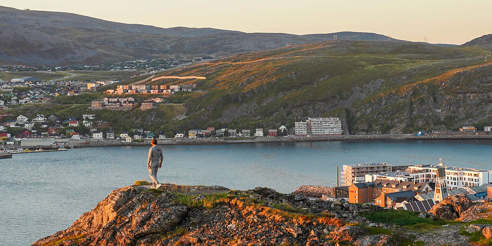 Man is standing at a cliff looking over Hammerfest, Norway, in the evening
