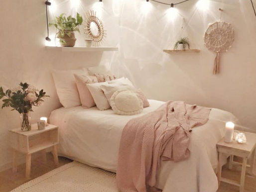 A bed decorated with pillows and a pink blanket, surrounded by candles and a bouquet of flowers