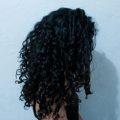 The back of a girl's black curly hair with a blue wall behind