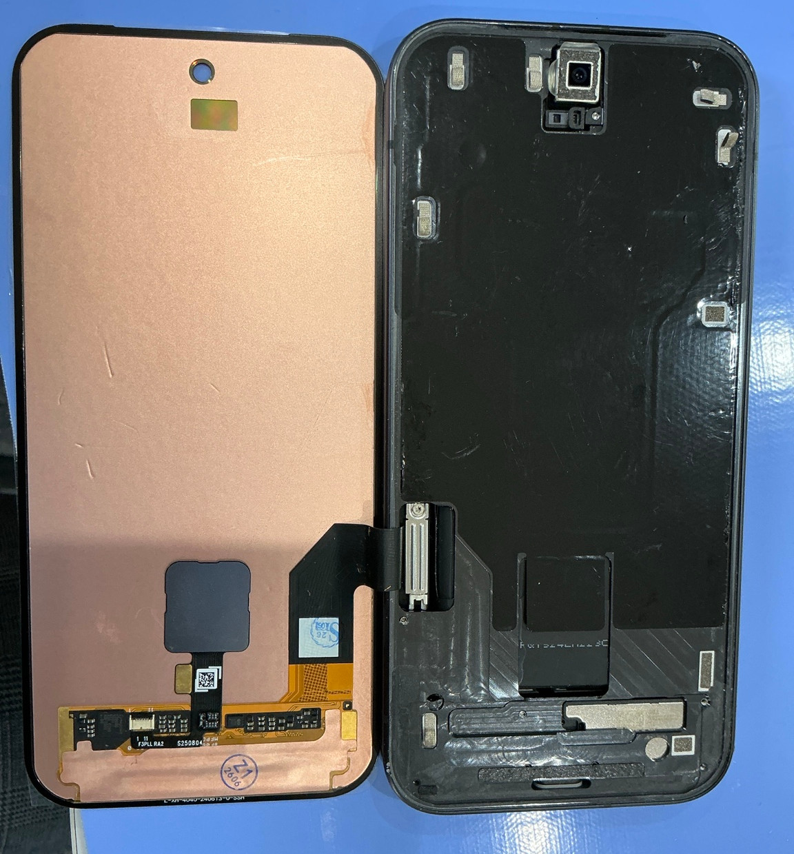 青い作業台の上に、分解されたスマホの画面部品2枚。左は金色の裏面、右は黒い裏面とカメラ部が見える修理中の様子】【。