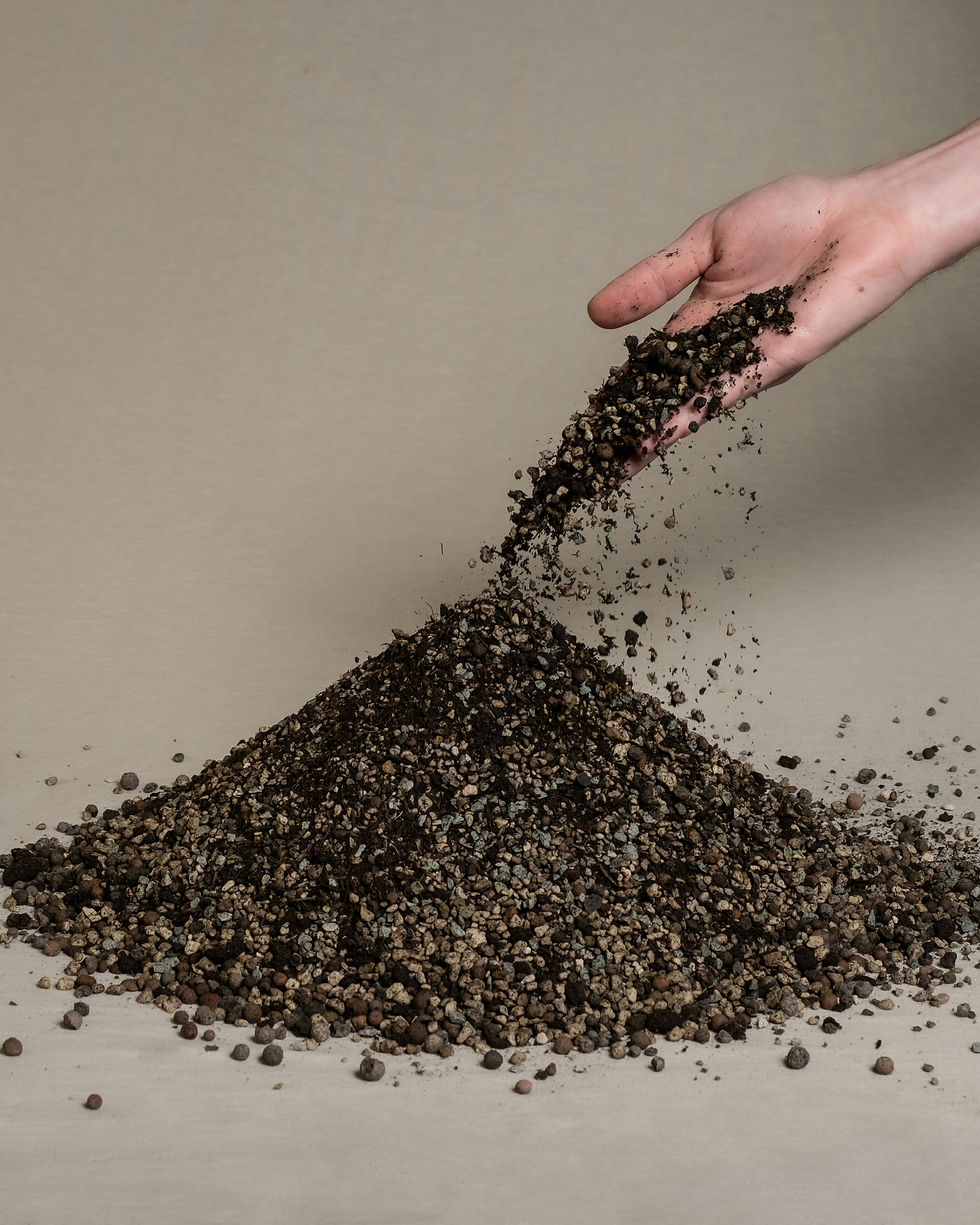 Hand pouring dirt and pebbles onto a small mound against a beige background, with soil scattering outward.