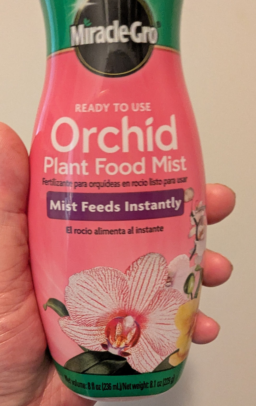 Hand holding a pink Miracle-Gro Ready to Use Orchid Plant Food Mist bottle with orchid image and visible label text on a plain background