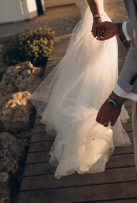 Bride holding grooms hand whilst walking into the golden sunshine on the coastal seaside of cyprus after their wedding