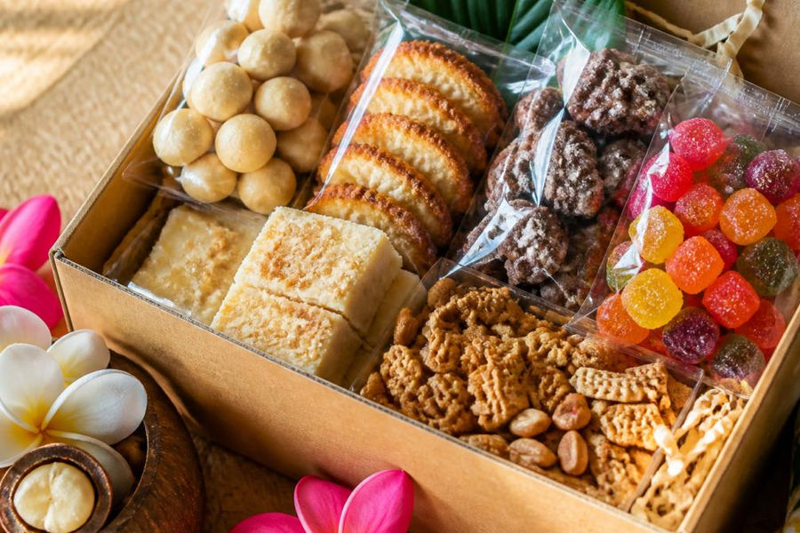 Close-up of colorful handcrafted island snacks including macadamia nuts, coconut treats, and artisanal gummies arranged in a gift box with natural lighting highlighting handcrafted textures and vibrant packaging
