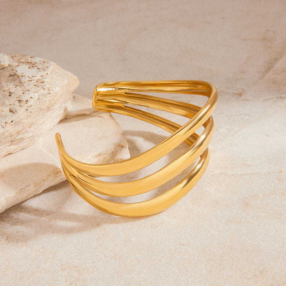 Golden cuff bracelet on a beige surface with a rock; 9to5Jewels.