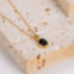 Gold necklace with black stone pendant on textured beige surface 9to5Jewels