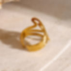 Gold ring with unique design on a textured cream colored surface.