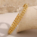 Gold-colored bracelet, detailed design, sitting on a textured surface, 9to5Jewels.