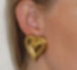 Woman wearing gold heart-shaped earrings, close up showcasing design and detail.