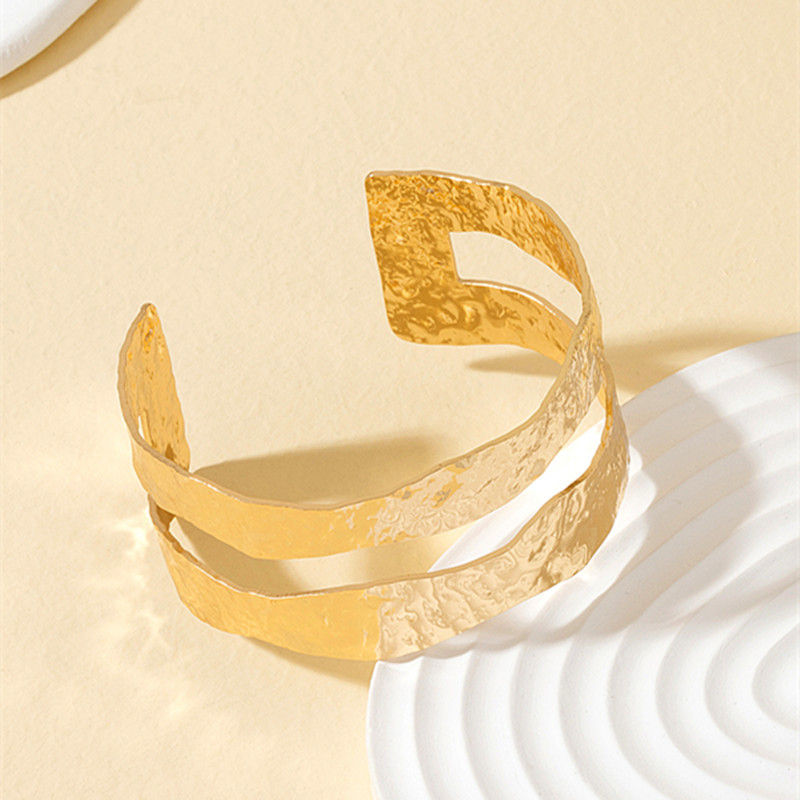 Gold cuff bracelet with a unique design over a beige background 9to5Jewels