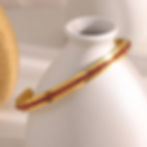 Gold bangle with red gemstones on a white vase, 9to5Jewels.