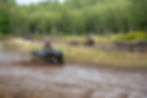 Three young four wheeler drivers riding through a muddy track spraying mud behind their ATV's