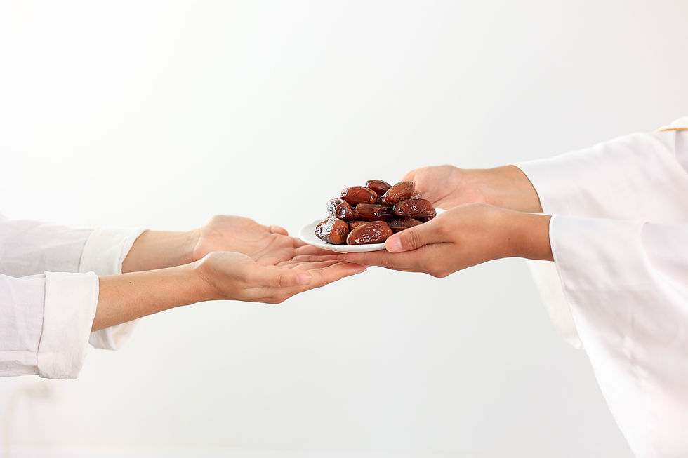 A person extending a small plate of dates to another person. Only their hands and forearms are visible and both are dressed in white.