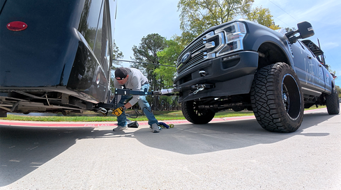 Man attaches wiring for tow bar cables to a black truck.