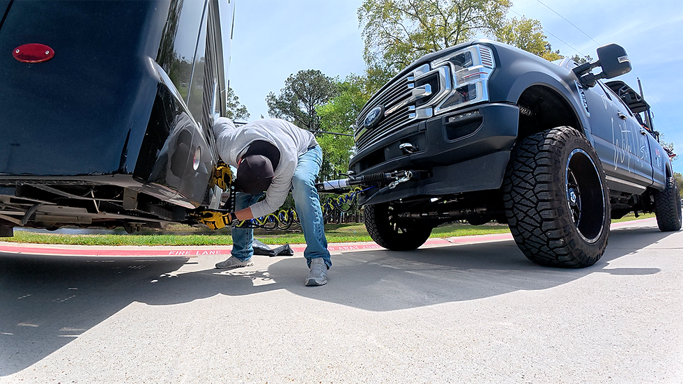 Man in jeans and cap attaches Demco Air Force One air hose to a large black F-250 truck. Sunny day, green trees in background.