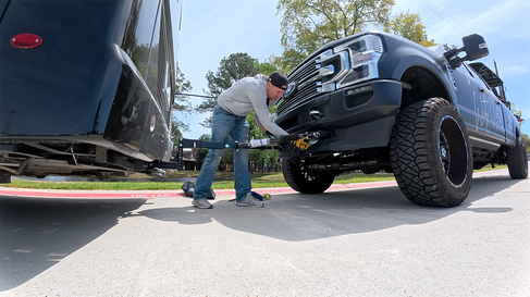 Man attached safety tow bar cables to a black truck.