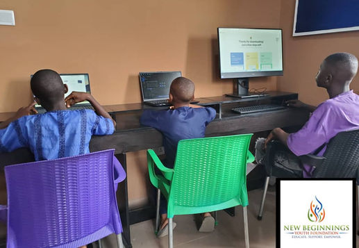 Three boys using computers in a room with brown walls. One large monitor displays a download message. Chairs are purple, green, and black.