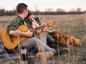 Una coppia con cane e chitarra che si rilassano all'aperto d'autunno su un prato